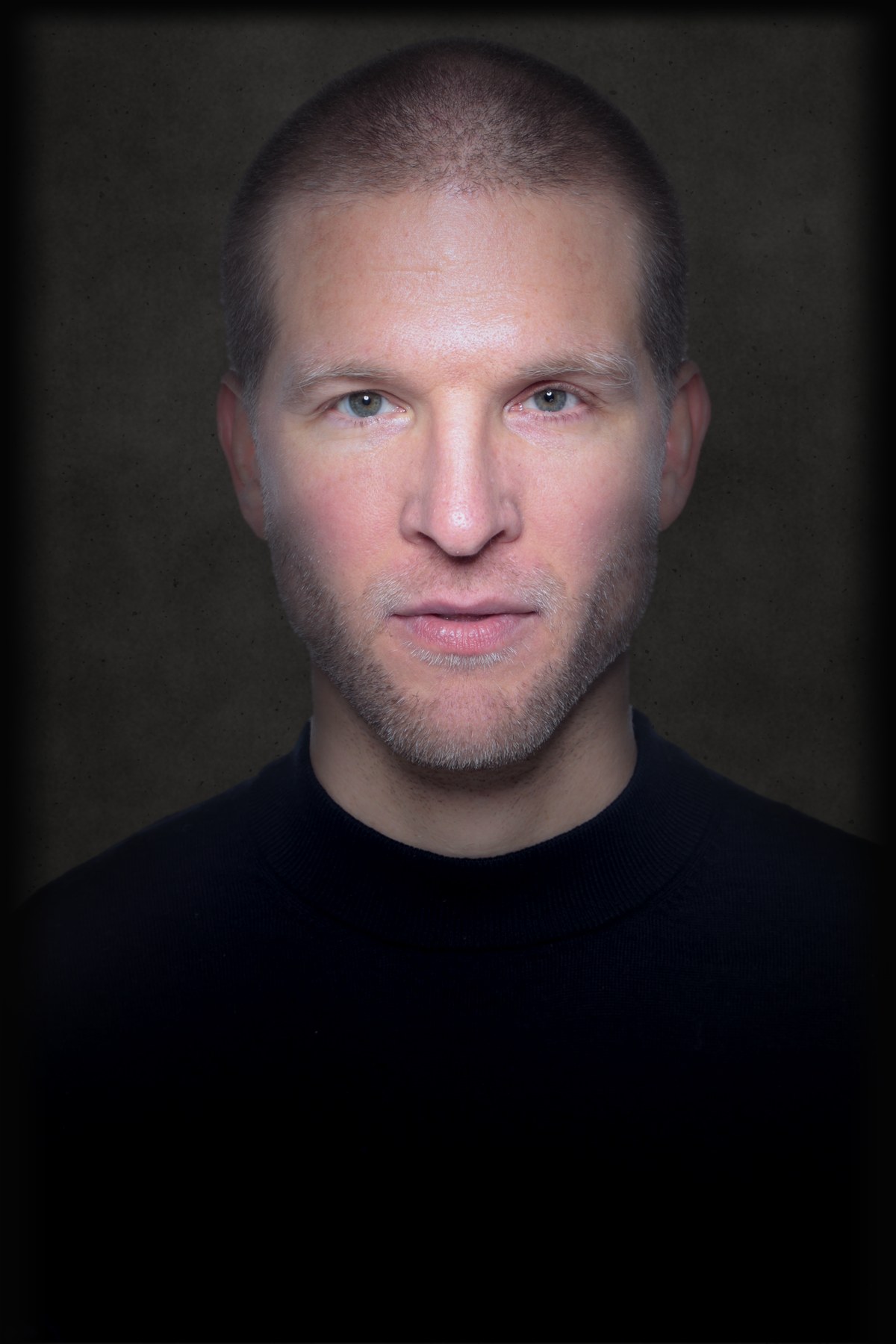 Portrait de Dominique Engelhardt, pull noir, fond béton gris foncé
