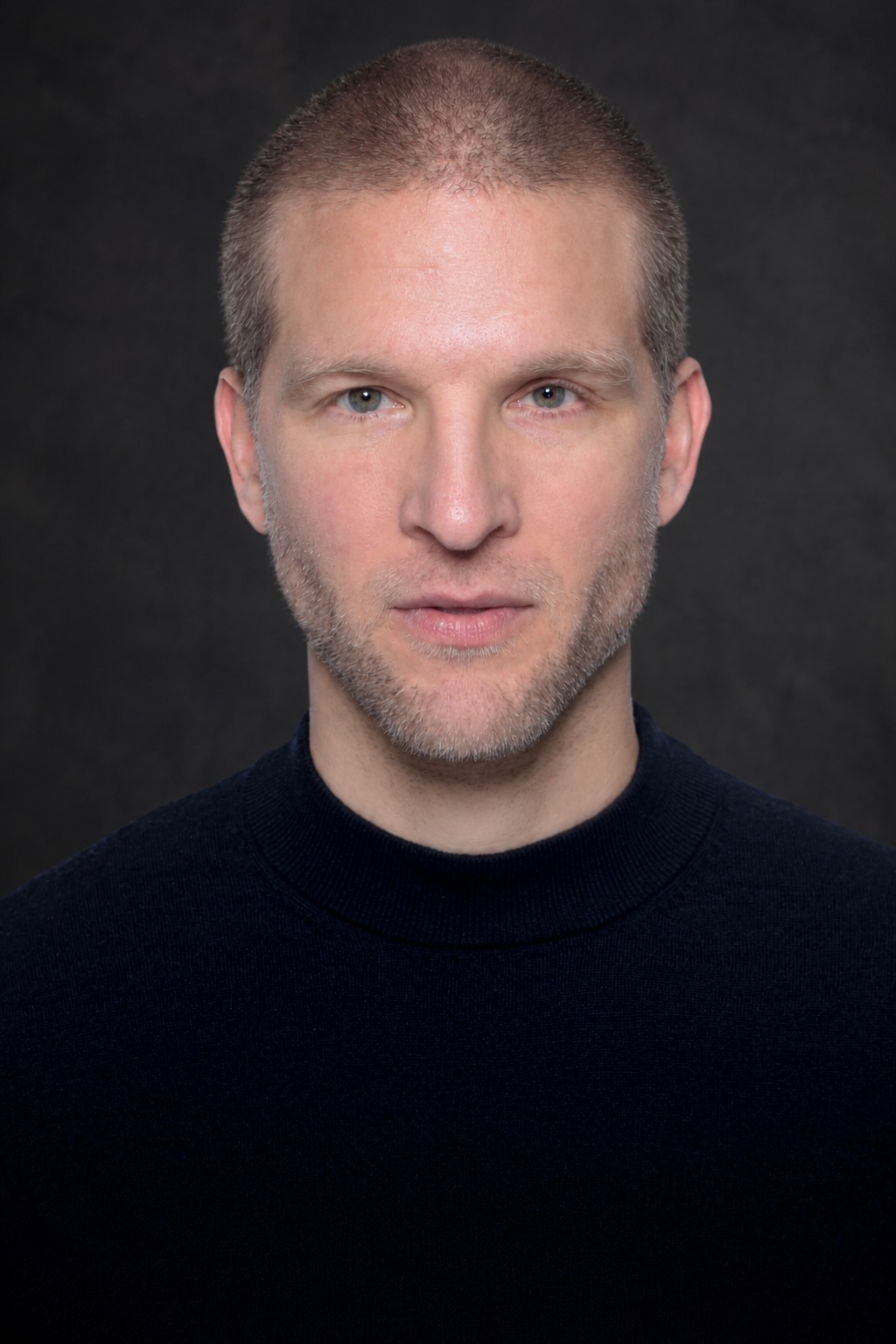 Portrait de Dominique Engelhardt, pull noir, fond béton gris foncé