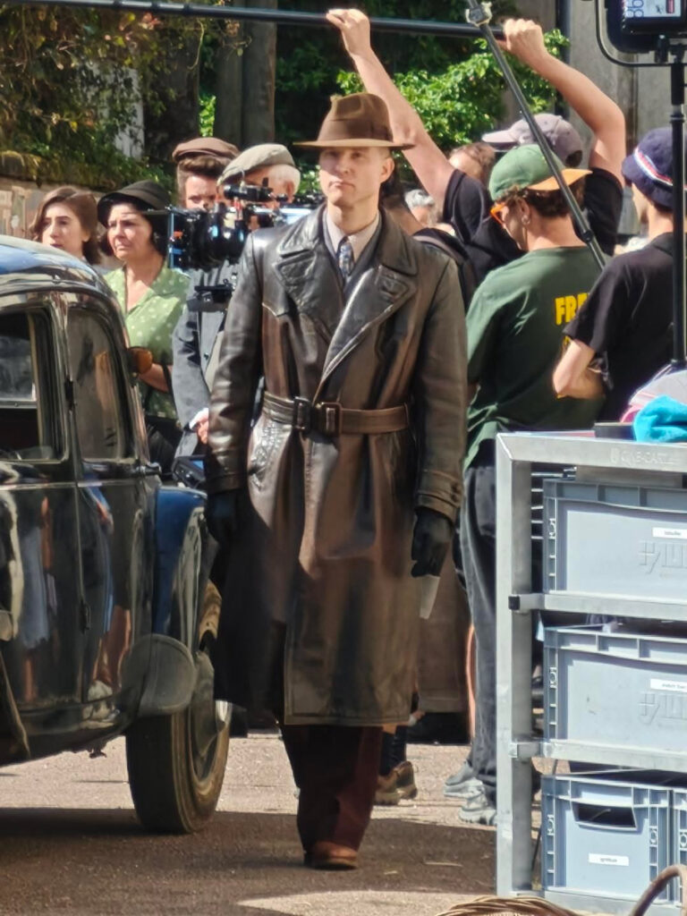 Sur un tournage, en manteau de cuir et chapeau, au milieu de l’équipe